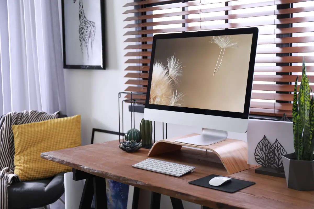 Modern home office with computer, office furniture, and wooden window blinds.